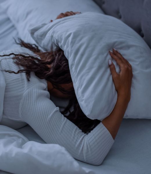 Sleeping Problem. Stressed African American lady lying alone in bed covering head under pillow feeling afraid or depressed, suffering from insomnia or mental problems after breakup